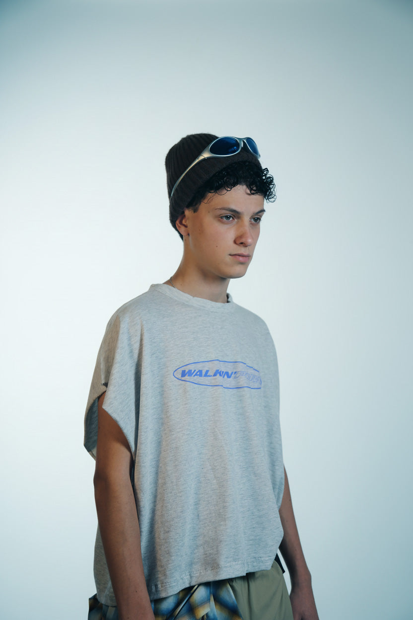 Person wearing a gray t-shirt with Walkin'Porn print and sunglasses on their head against a plain background
