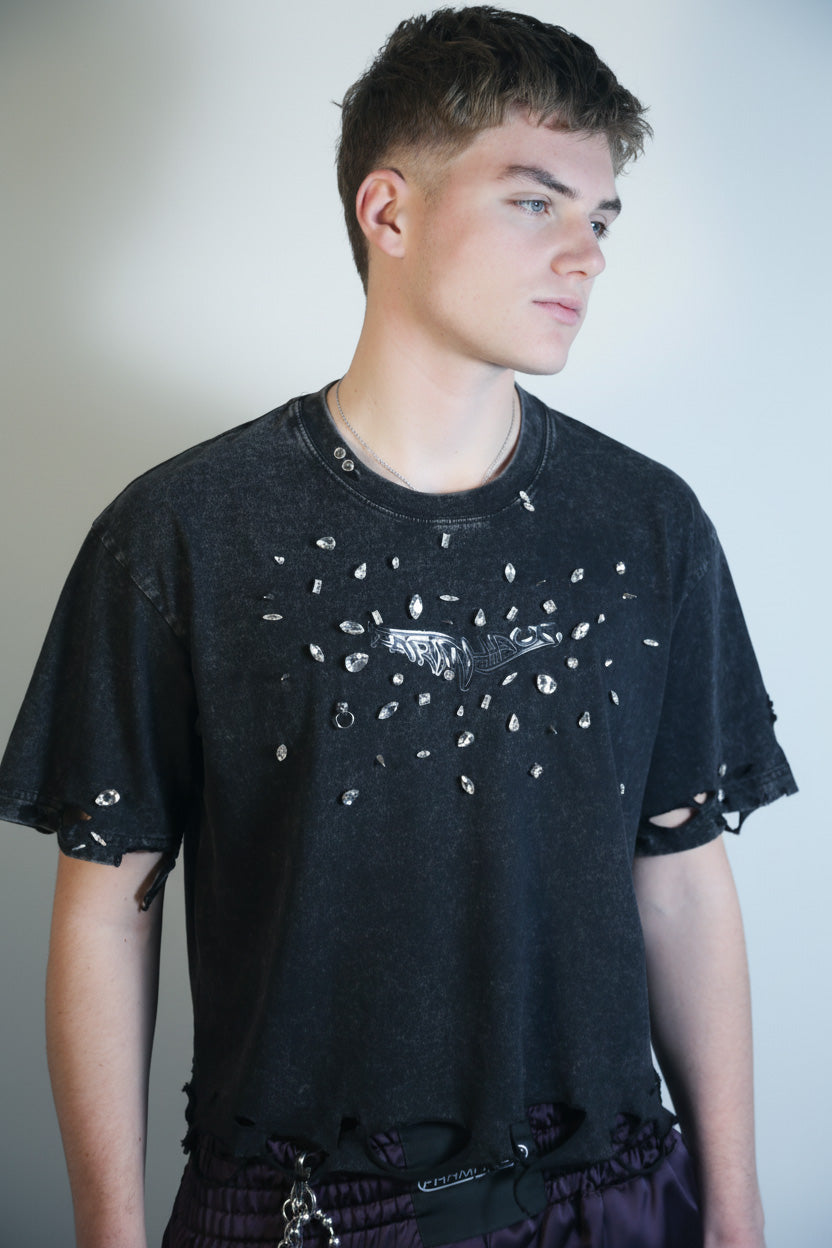 Model wearing a black distressed t-shirt with crystal and studs against a plain background