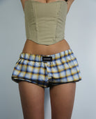 Person wearing a green top and plaid shorts with a visible brand label on a gray background