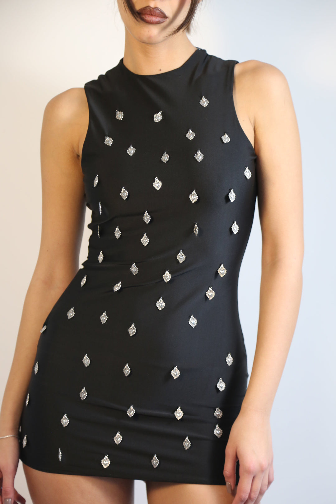 Black dress with white ex voto charms worn by a model on a plain background