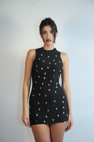 Woman wearing a black dress with ex voto charms against a plain background