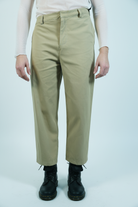 Beige pants worn by a person on a white background, asymmetrical waist 