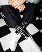 Person wearing plaid pants and white sneakers with black and white socks on a checkered floor.
