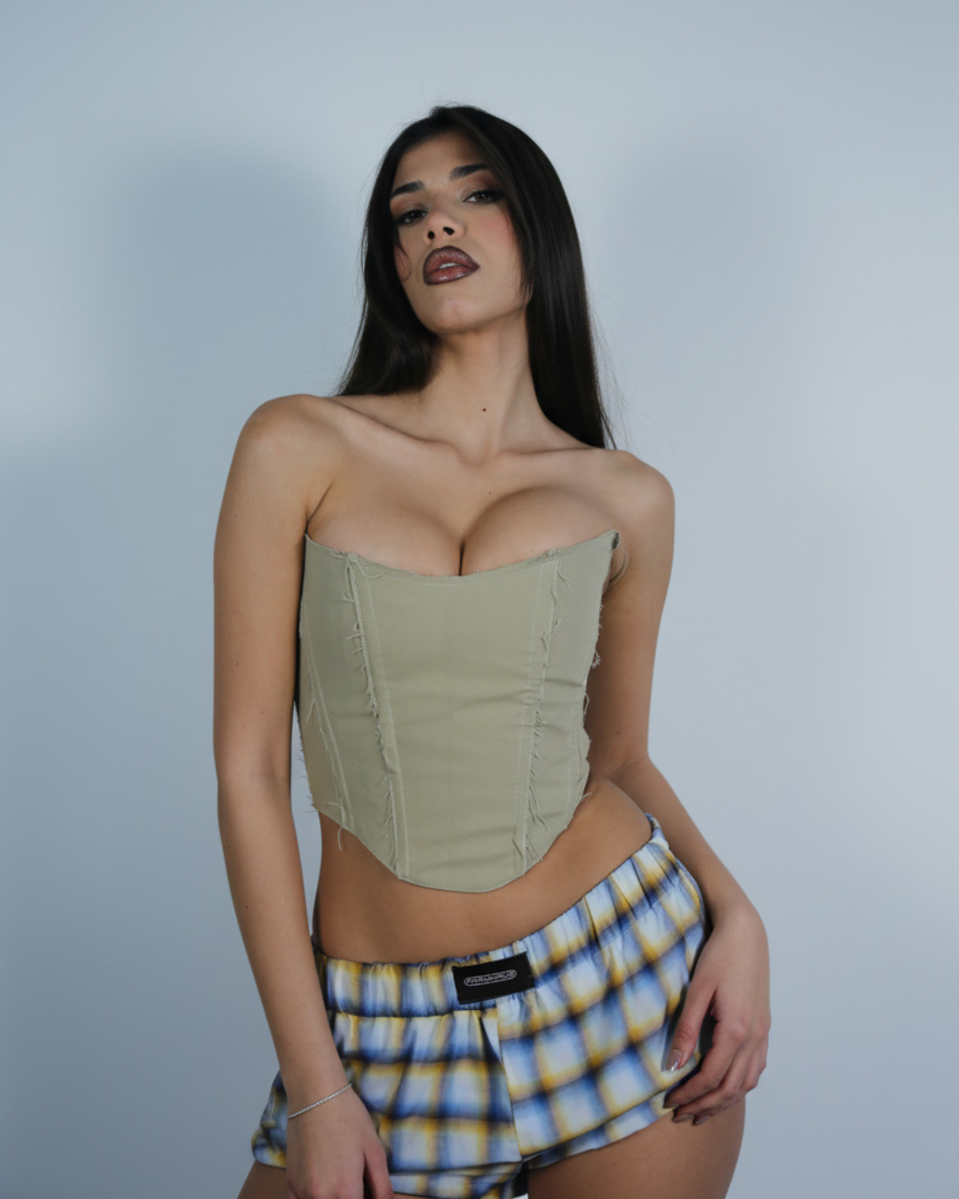 Model wearing a strapless corset and plaid shorts against a plain background