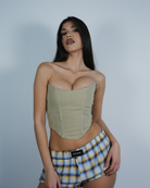 Model wearing a strapless corset and plaid shorts against a plain background