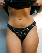 Black bikini bottom with embellishments on a neutral background